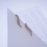 Load image into Gallery viewer, A pair of gold and silver wavy crescent-shaped earrings with clear pavé stones, displayed on a white geometric card.