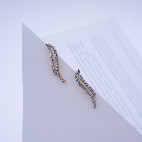 A pair of gold and silver wavy crescent-shaped earrings with clear pavé stones, displayed on a white geometric card.